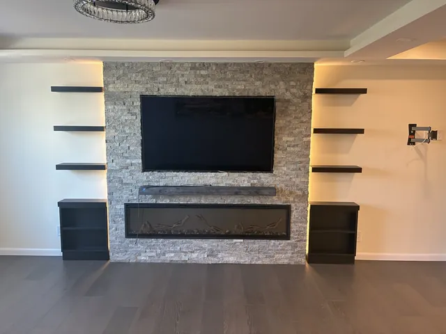 Stacked-stone fireplace wall with a TV and floating shelves